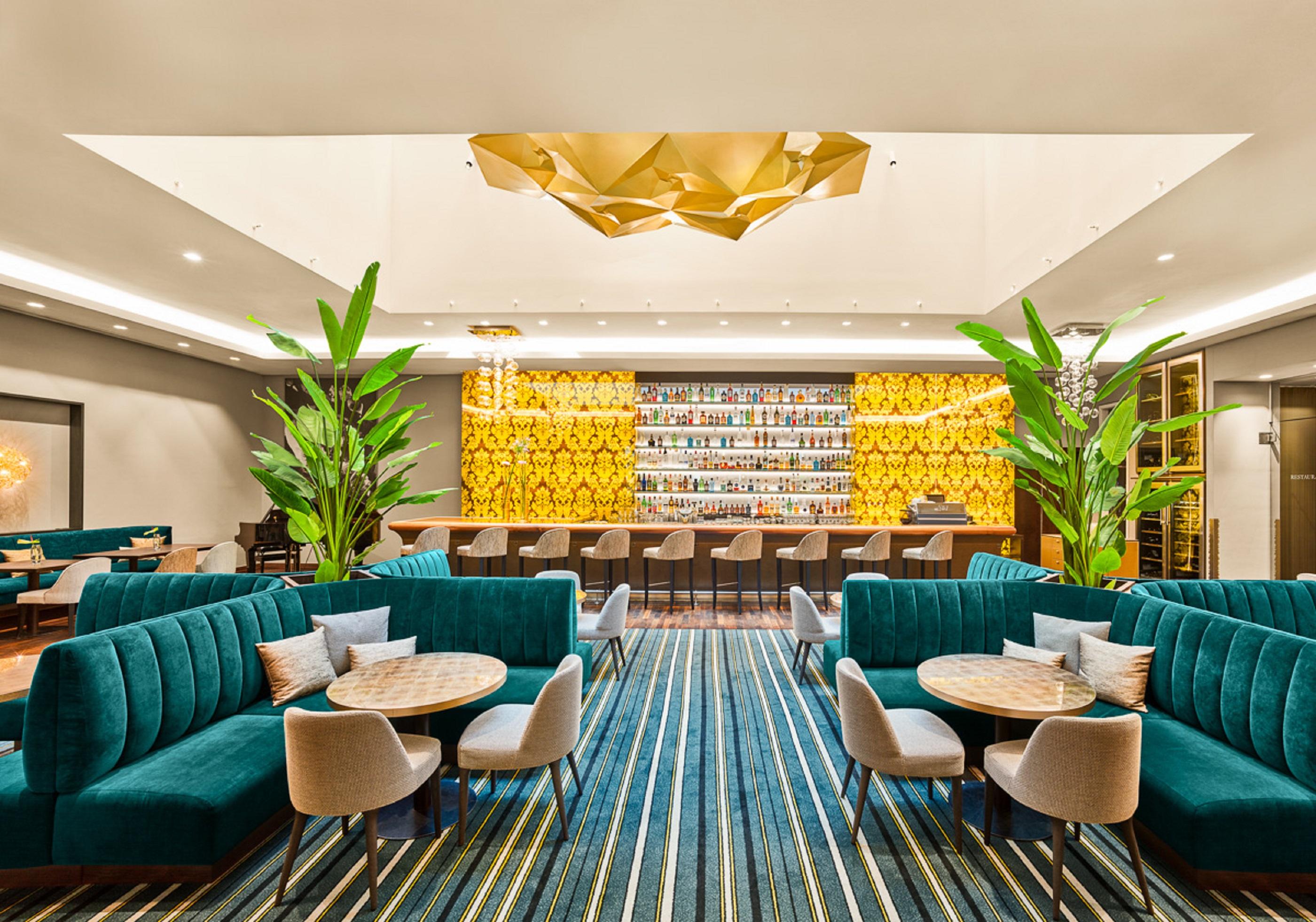 Steigenberger Hotel Herrenhof Вена Экстерьер фото The photo shows a modern lounge or bar area featuring stylish teal seating arrangements, including plush sofas and round tables. In the background, there is a well-lit bar decorated with a vibrant yellow wall, adorned with various bottles. The space 