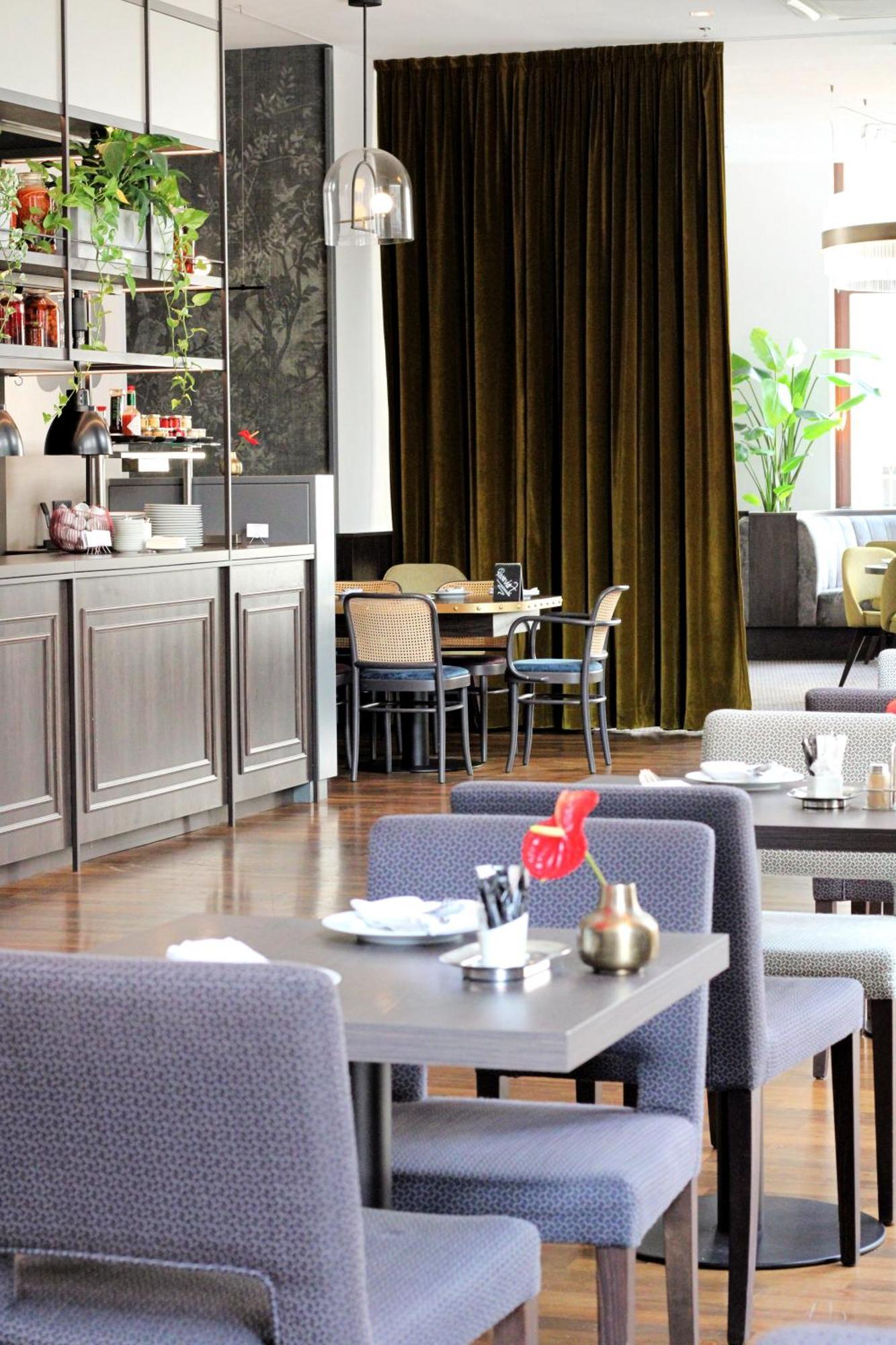 Steigenberger Hotel Herrenhof Вена Экстерьер фото The photo depicts the interior of a restaurant or café. It features a stylish design with wooden flooring and a modern aesthetic. In the foreground, there are tables set for dining, some with decorative items like flowers. To the side, there is a bar